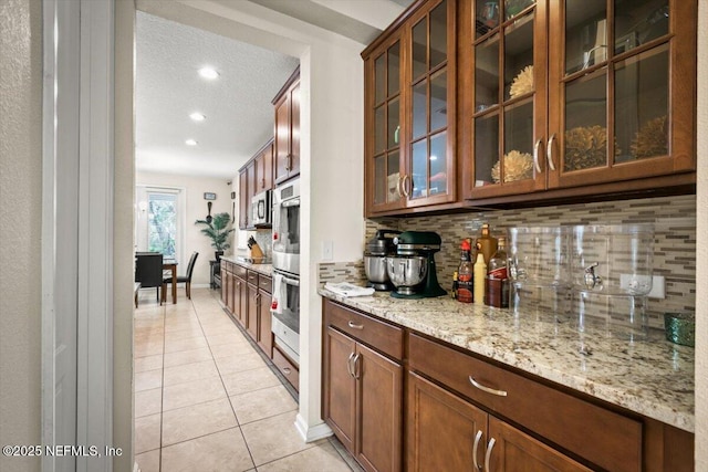 bar with light stone countertops, stainless steel double oven, a textured ceiling, decorative backsplash, and light tile patterned floors