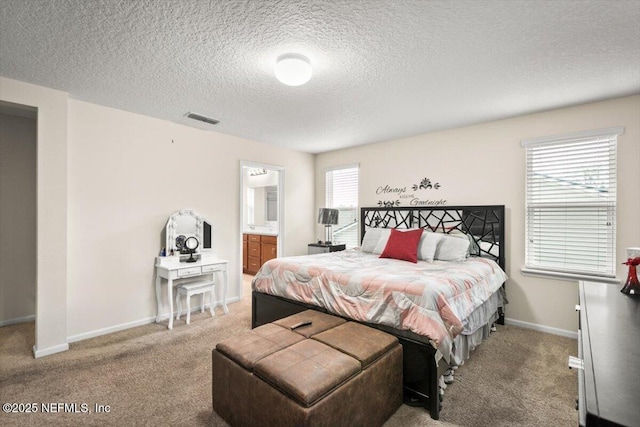 bedroom with a textured ceiling, connected bathroom, and light colored carpet