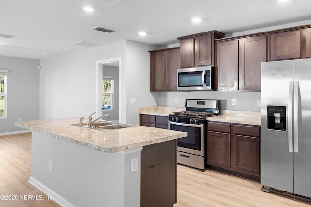 kitchen featuring sink, stainless steel appliances, an island with sink, light hardwood / wood-style floors, and a textured ceiling