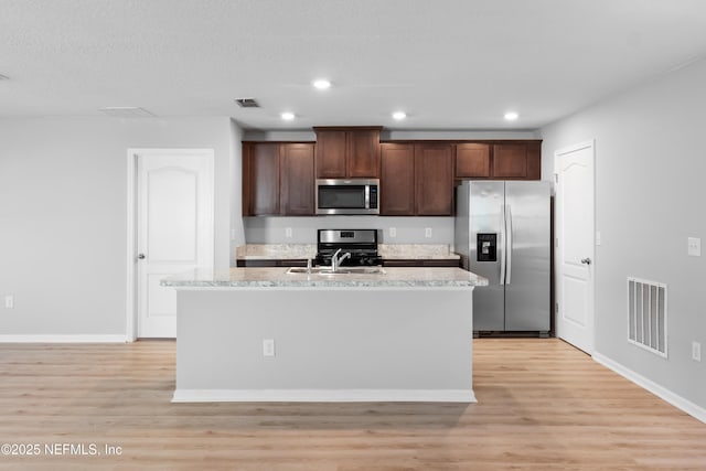 kitchen featuring dark brown cabinetry, light hardwood / wood-style flooring, an island with sink, and stainless steel appliances