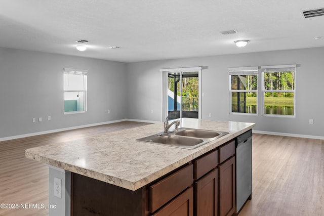 kitchen with light wood-type flooring, stainless steel dishwasher, dark brown cabinets, sink, and an island with sink