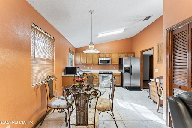 kitchen with a textured ceiling, vaulted ceiling, pendant lighting, appliances with stainless steel finishes, and light tile patterned flooring