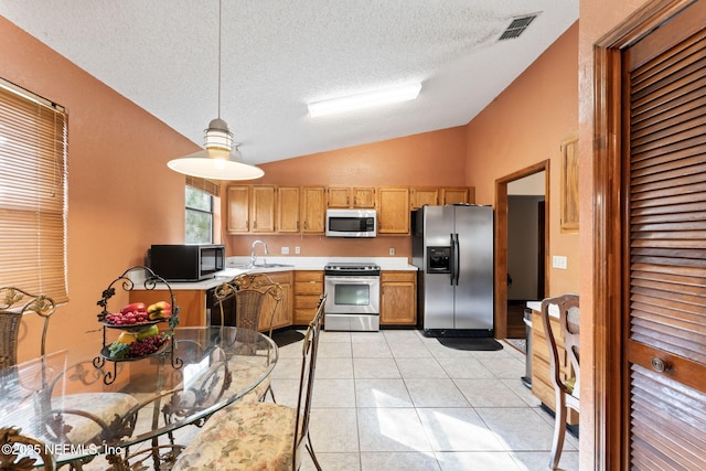 kitchen with sink, decorative light fixtures, vaulted ceiling, light tile patterned floors, and appliances with stainless steel finishes