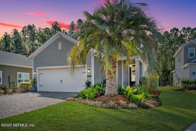 view of front of property featuring an attached garage, decorative driveway, and a yard