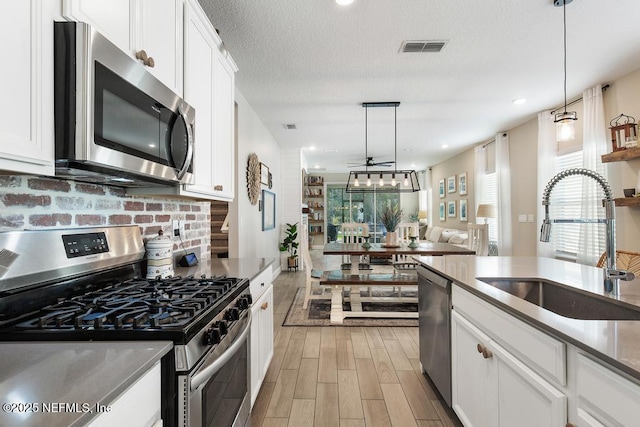 kitchen featuring sink, white cabinets, hanging light fixtures, and appliances with stainless steel finishes