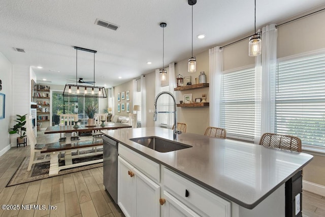 kitchen featuring white cabinetry, sink, hanging light fixtures, stainless steel dishwasher, and an island with sink