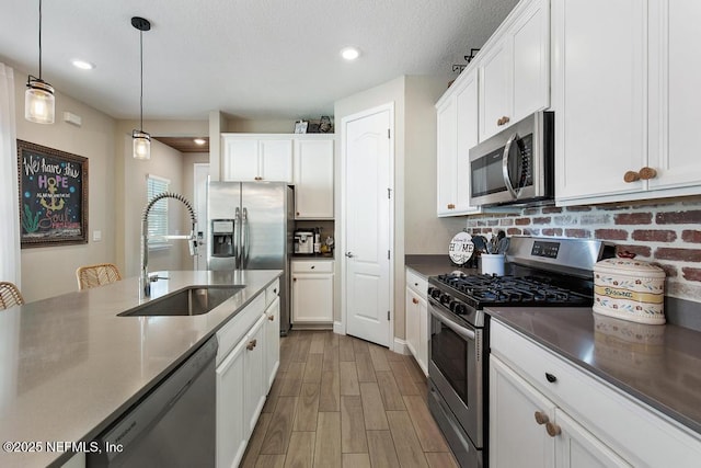 kitchen featuring stainless steel appliances, hanging light fixtures, white cabinets, a sink, and wood finished floors