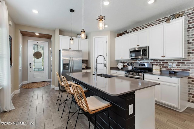 kitchen with sink, an island with sink, decorative light fixtures, a kitchen bar, and appliances with stainless steel finishes