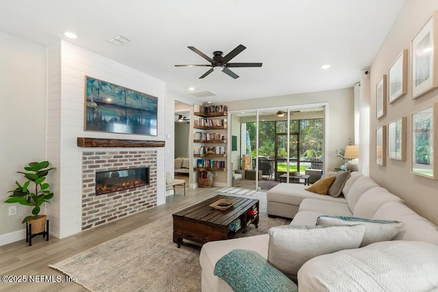 living room featuring a brick fireplace, ceiling fan, and light hardwood / wood-style flooring