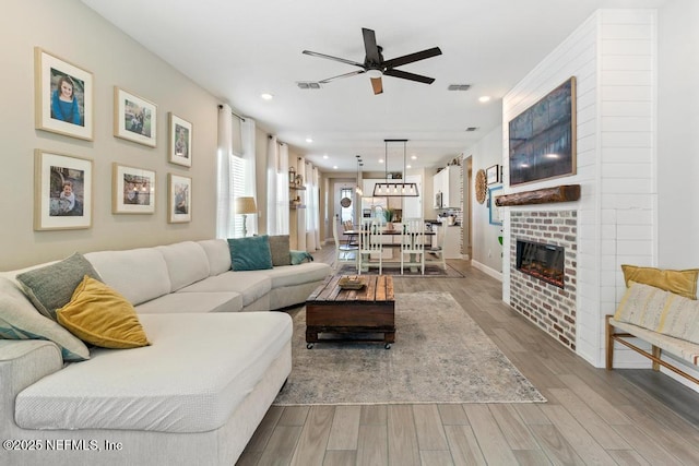 living room featuring a fireplace, light hardwood / wood-style floors, and ceiling fan