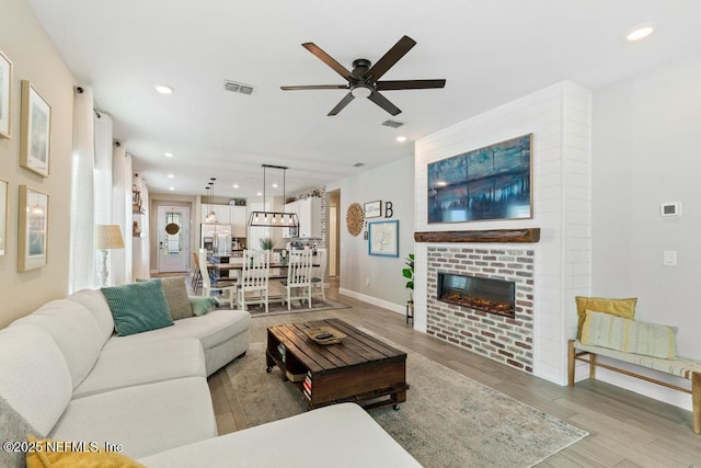 living room featuring ceiling fan, a fireplace, and light hardwood / wood-style floors