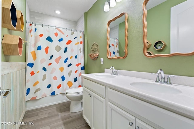 full bathroom with double vanity, toilet, a sink, and wood finish floors