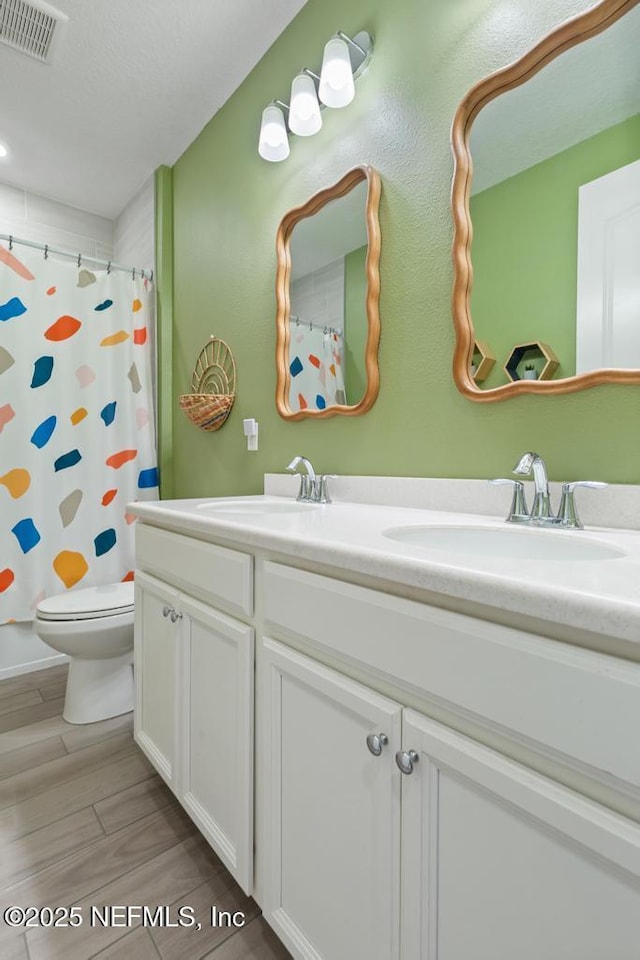 full bath with toilet, a sink, visible vents, wood tiled floor, and double vanity