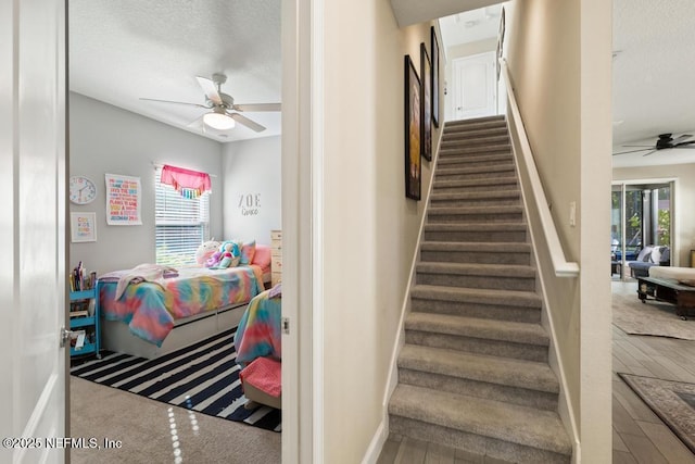 stairs featuring ceiling fan, a textured ceiling, baseboards, and wood finished floors