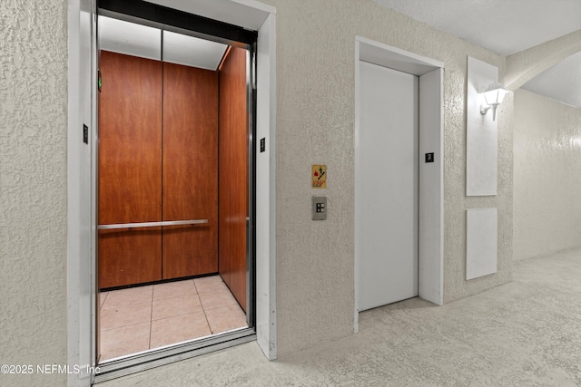 hall with elevator and light colored carpet