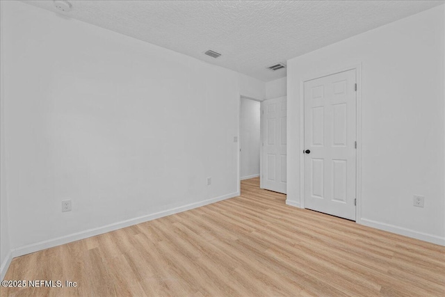 empty room with a textured ceiling and light hardwood / wood-style flooring