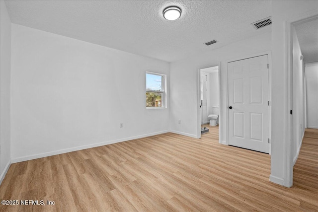 unfurnished bedroom with a textured ceiling, connected bathroom, and light wood-type flooring