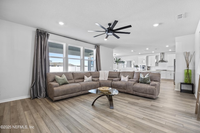 living room with ceiling fan, light wood-type flooring, and a textured ceiling