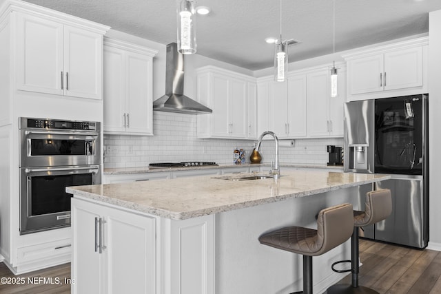 kitchen featuring decorative light fixtures, wall chimney range hood, white cabinets, and stainless steel appliances