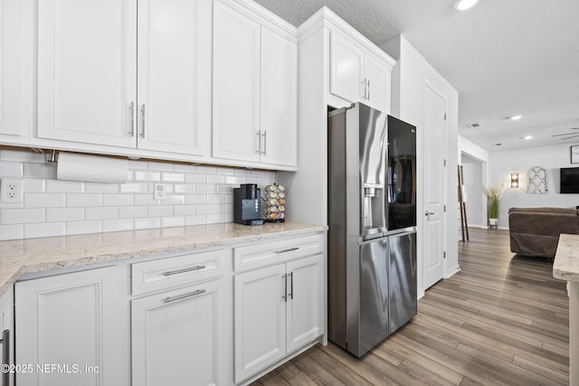 kitchen with white cabinetry, stainless steel refrigerator with ice dispenser, tasteful backsplash, light hardwood / wood-style flooring, and light stone counters