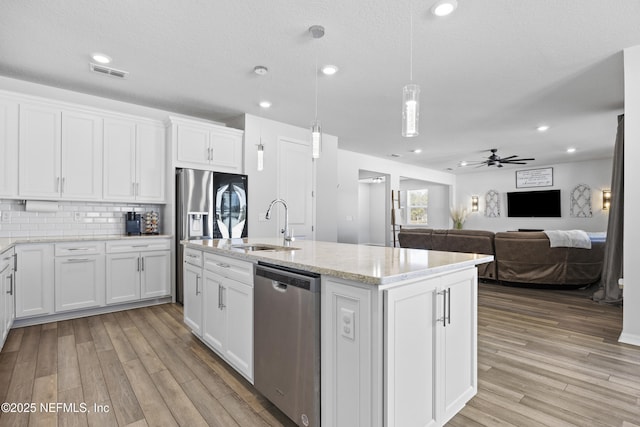 kitchen featuring a center island with sink, ceiling fan, stainless steel appliances, pendant lighting, and white cabinets