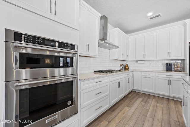 kitchen with backsplash, wall chimney exhaust hood, stainless steel appliances, and white cabinetry