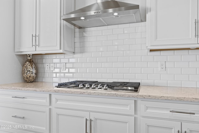 kitchen with decorative backsplash, white cabinetry, stainless steel gas stovetop, and wall chimney exhaust hood