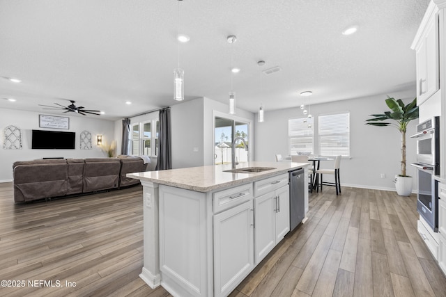 kitchen with ceiling fan, a center island with sink, sink, appliances with stainless steel finishes, and white cabinets