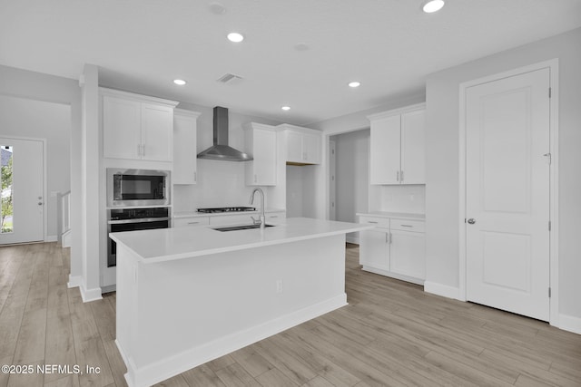 374 Sutton Dr, Ponte Vedra, FL 32081 - kitchen with wall chimney exhaust hood, stainless steel appliances, light wood-type flooring, white cabinetry, and a kitchen island with sink
