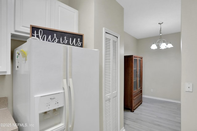 kitchen with white refrigerator with ice dispenser, pendant lighting, white cabinets, and an inviting chandelier