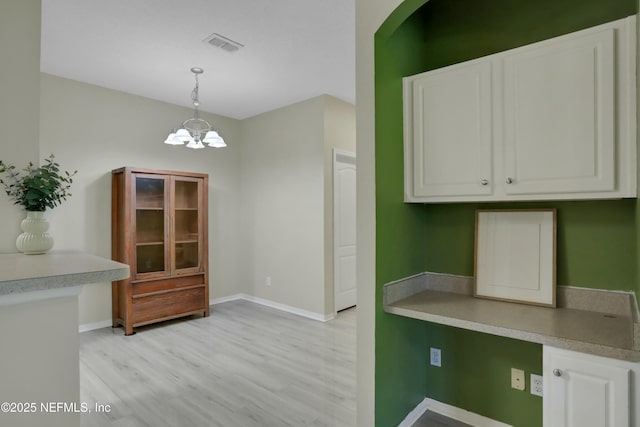 kitchen featuring pendant lighting, white cabinets, light wood-type flooring, and a chandelier