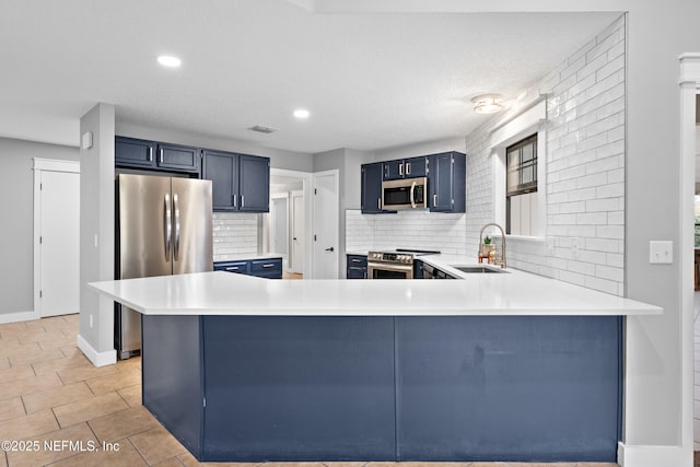 kitchen featuring sink, tasteful backsplash, kitchen peninsula, blue cabinetry, and appliances with stainless steel finishes