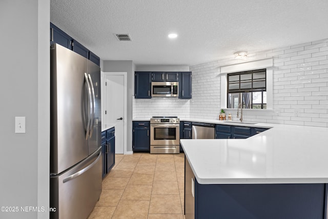 kitchen featuring appliances with stainless steel finishes, blue cabinetry, sink, and kitchen peninsula