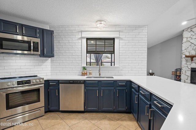 kitchen with appliances with stainless steel finishes, blue cabinetry, light tile patterned flooring, and sink