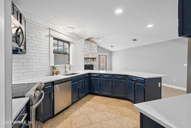 kitchen featuring kitchen peninsula, stainless steel appliances, lofted ceiling, blue cabinetry, and sink