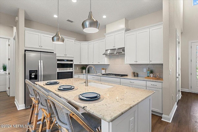 kitchen with appliances with stainless steel finishes, a breakfast bar, decorative light fixtures, light stone counters, and a center island with sink