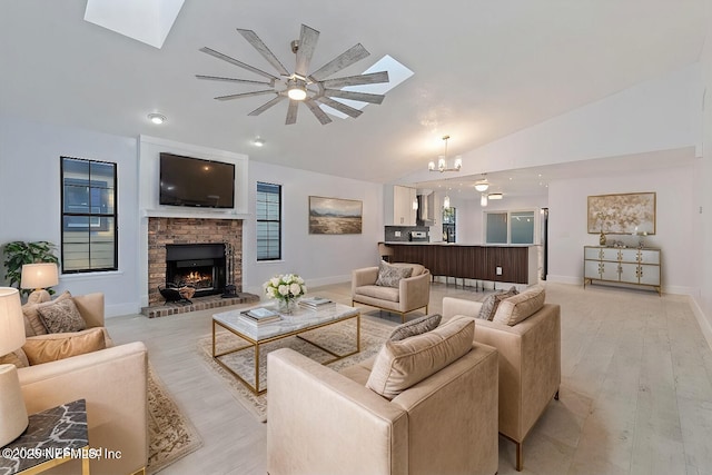 living room with ceiling fan with notable chandelier, lofted ceiling with skylight, and light hardwood / wood-style flooring