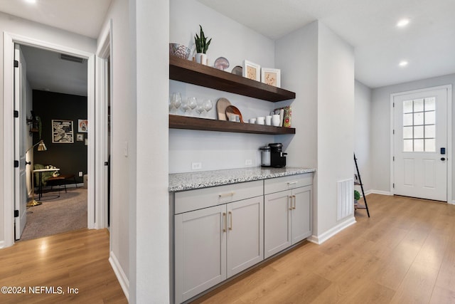 bar with gray cabinets, light stone countertops, and light hardwood / wood-style flooring