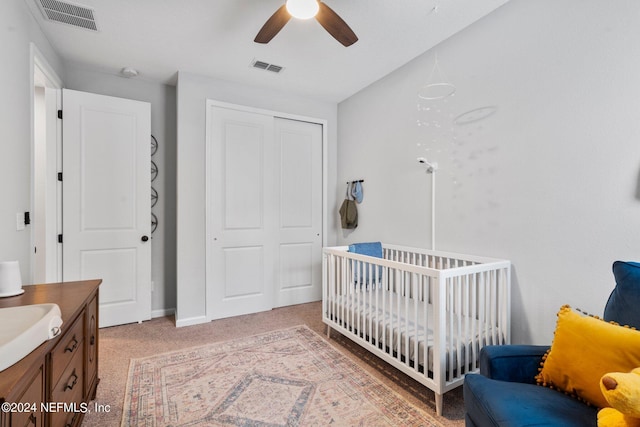 carpeted bedroom with ceiling fan, a crib, and a closet