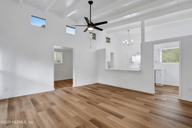 unfurnished living room with beamed ceiling, a high ceiling, ceiling fan with notable chandelier, and light hardwood / wood-style floors