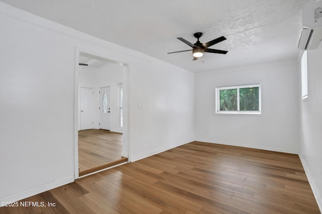 unfurnished room featuring hardwood / wood-style floors, a textured ceiling, an AC wall unit, and ceiling fan