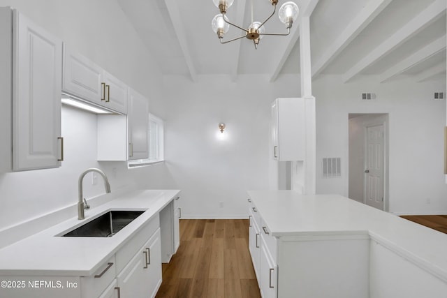 kitchen featuring white cabinetry, sink, an inviting chandelier, beamed ceiling, and pendant lighting