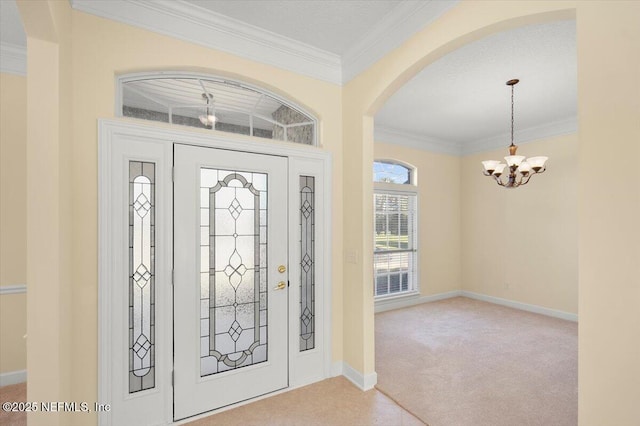 carpeted foyer featuring ornamental molding and a chandelier