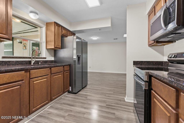 kitchen with light hardwood / wood-style floors, dark stone countertops, sink, and appliances with stainless steel finishes