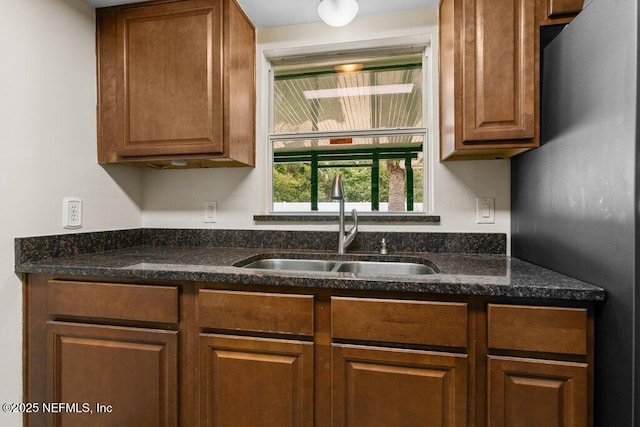 kitchen with stainless steel refrigerator, sink, and dark stone countertops