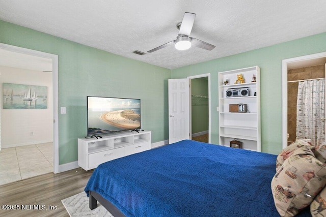 bedroom featuring a walk in closet, a textured ceiling, ceiling fan, hardwood / wood-style flooring, and a closet