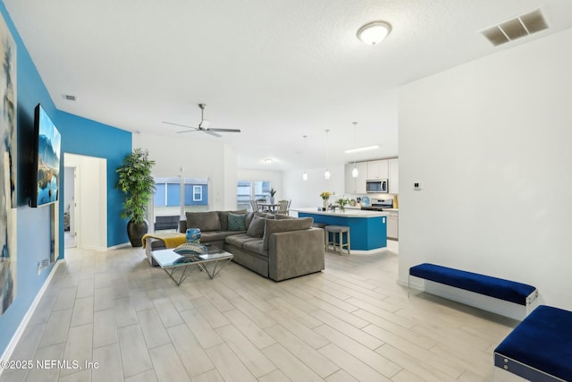 living room with ceiling fan, a textured ceiling, and light hardwood / wood-style flooring