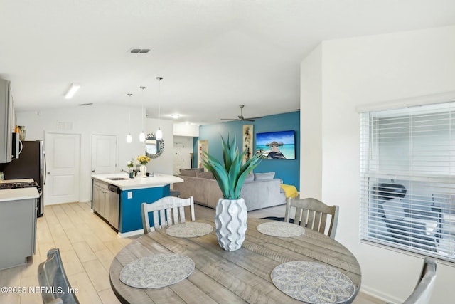 dining room featuring ceiling fan, vaulted ceiling, sink, and light hardwood / wood-style floors