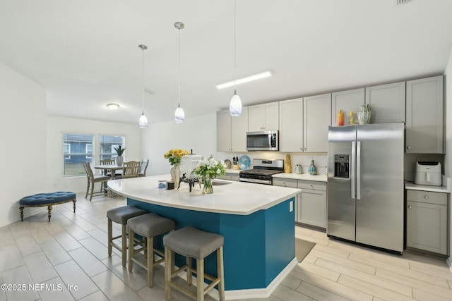 kitchen with decorative light fixtures, a kitchen island with sink, gray cabinetry, and stainless steel appliances