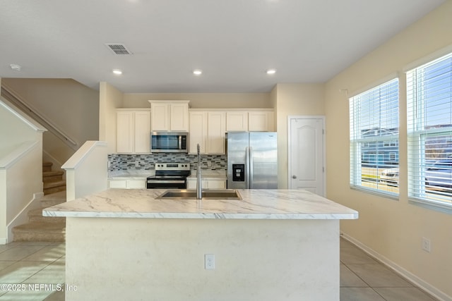 kitchen featuring appliances with stainless steel finishes, sink, light tile patterned floors, a center island with sink, and white cabinets